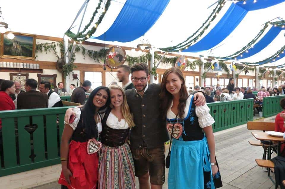 Three girls and one guy wearing traditional Oktoberfest gear in a tent in Munich, Germany.