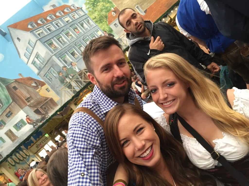 Three people posing for a picture at Oktoberfest as they sport their traditional liederhosn and dirndls.