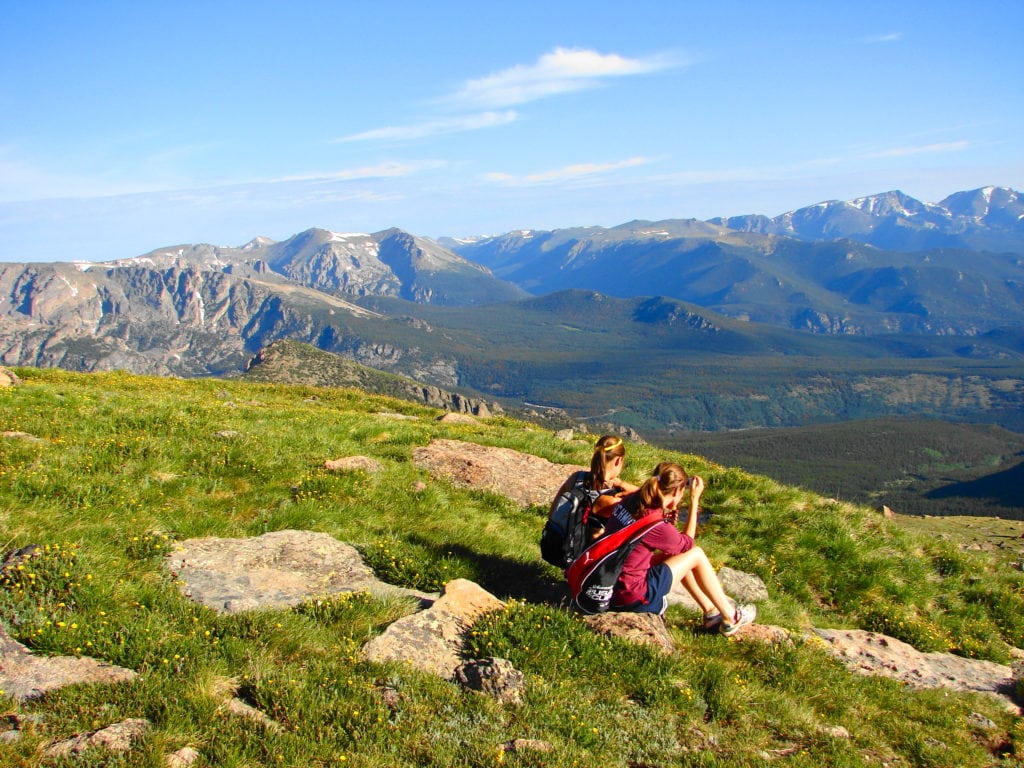 Two hikers sitting in the grass gazing out into Rocky Mountain National Park from the side of Long's Peak.