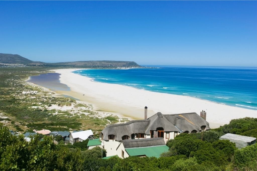 A Long Stretch of Long Beach With a House in the Foreground. One of the Best Beaches in Cape Town.