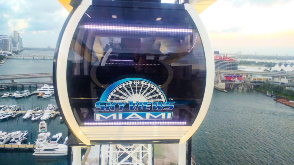 A glass gondola on the Miami Skyviews Observation Wheel with city views and boats in the distance.