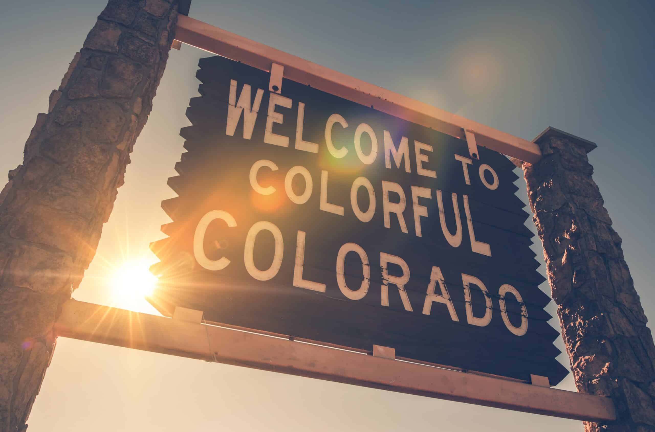 A picture of the Welcome To Colorful Colorado sign with the sun peaking in from behind.