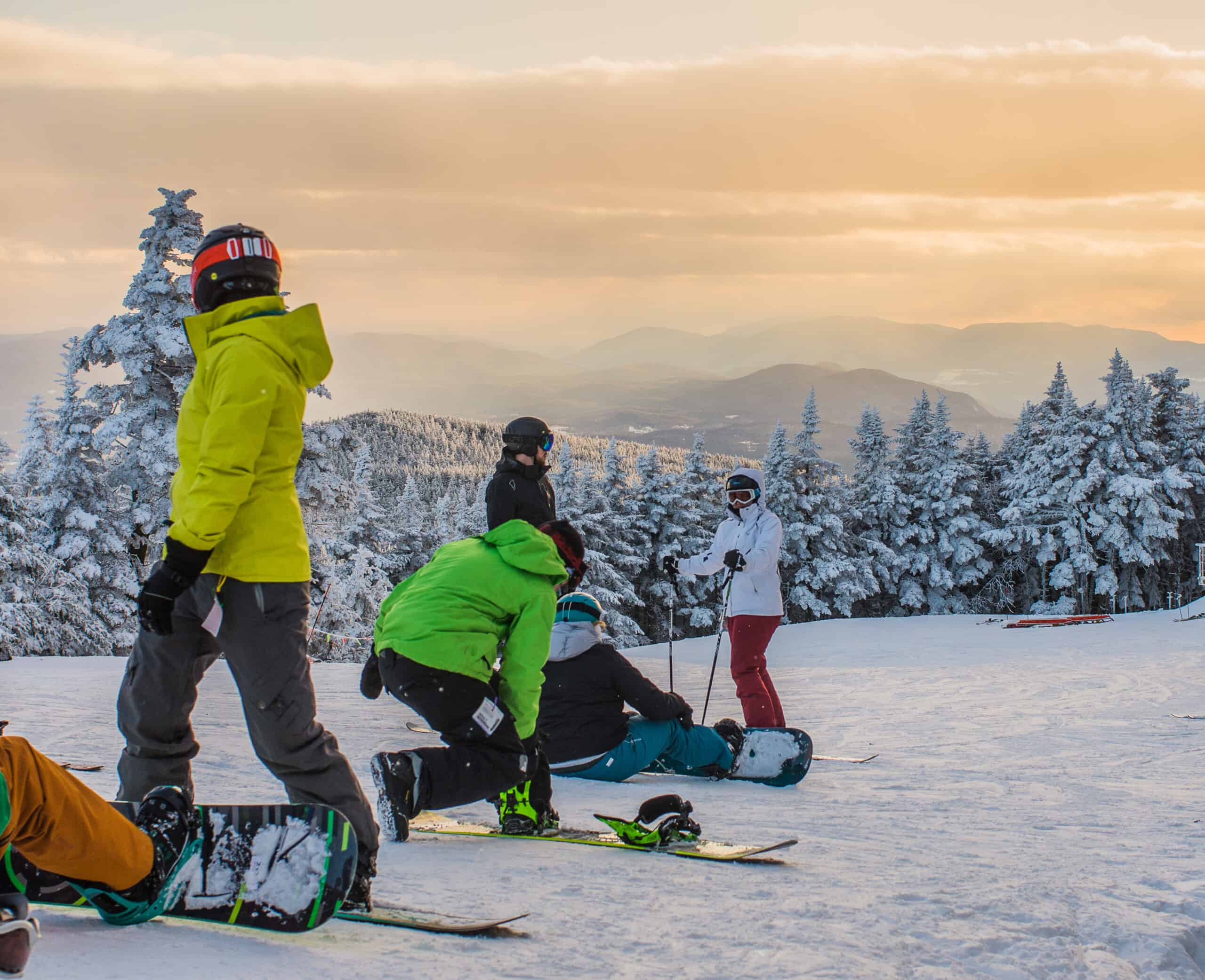 Snowboarders sitting on the mountain at sunset.