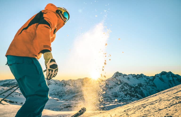 A picture of a skier as the sun is setting. They are flicking snow into the air and it's catching the sun rays in a unique way.