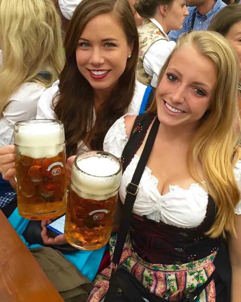 Two girls wearing dirndls at Oktoberfest in Munich, Germany with steins of beer.