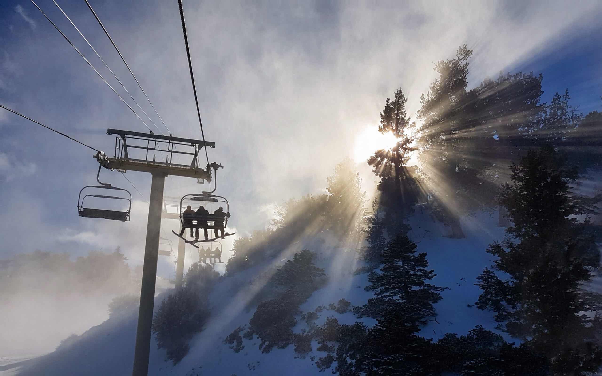 The sun breaks through trees as a chairlift takes skiers up Copper Mountain.