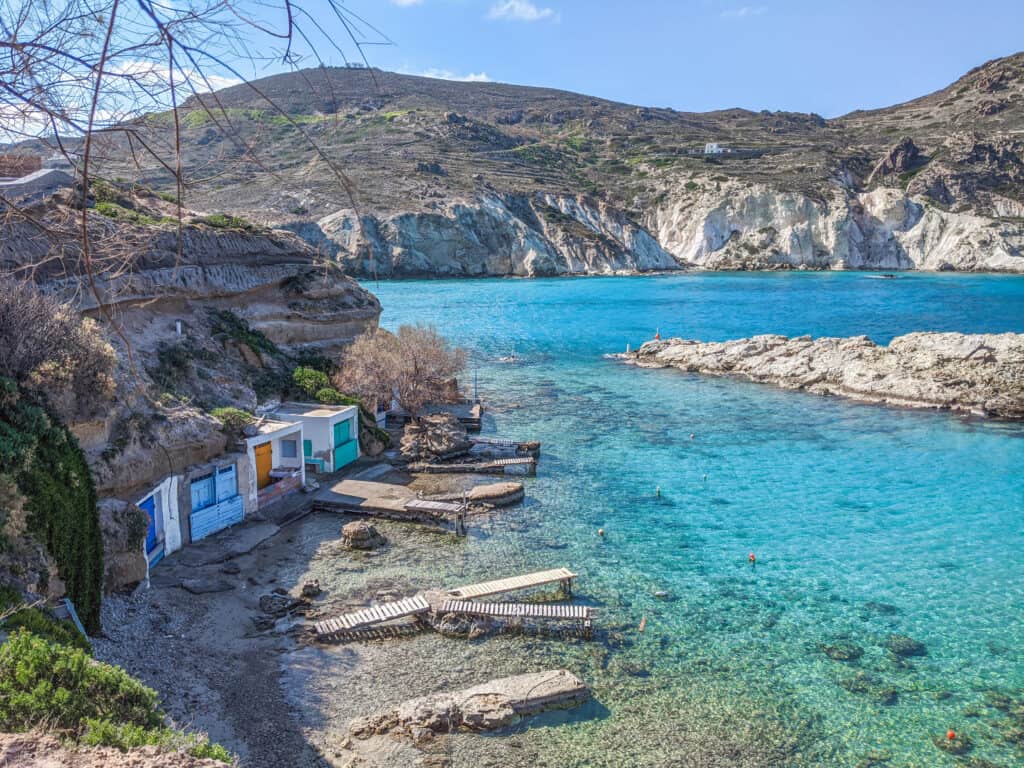 A picture of the blue ocean in Milos, Greece with boathouses on the shore.