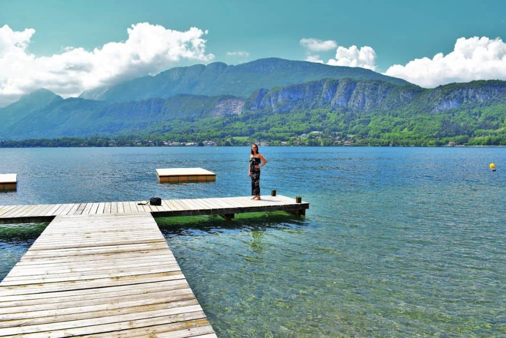 Emily standing on a dock extended over a lake with beautiful rolling hills and mountains behind her.